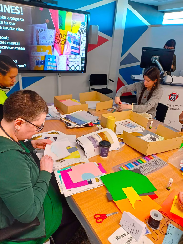 Participants on our Mad Studies course. People sit around a table working with brightly coloured craft materials.